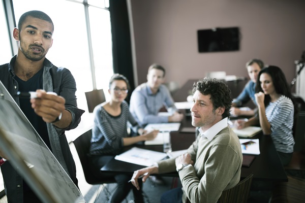 Project team member gesturing to whiteboard in a team meeting